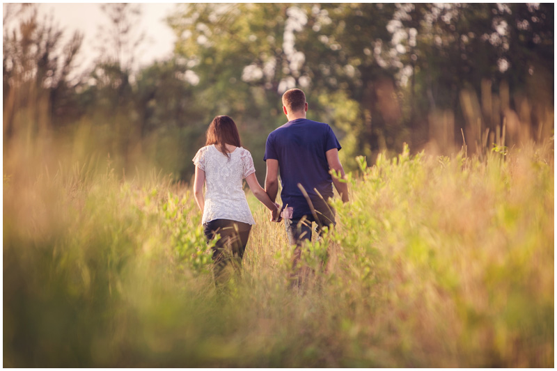 A cute couple walks hand in hand in a gorgeous summer field in North Carolina by Mabyn Ludke Photography