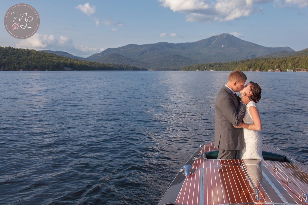 A bride and groom kiss while enjoying their hacker craft boat ride on Lake Placid. Mabyn Ludke Photography