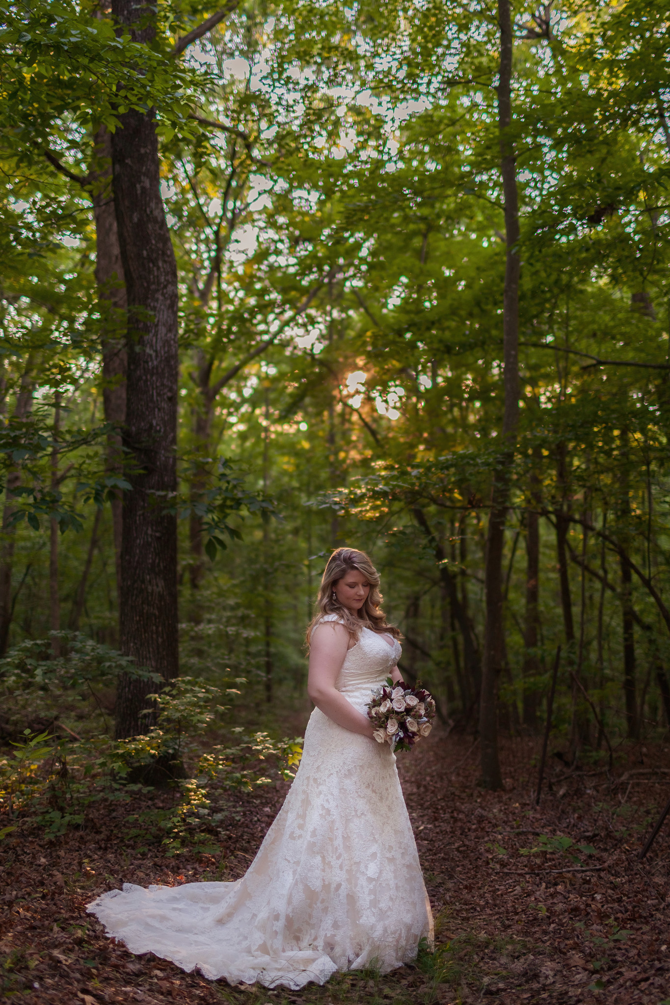 This beautiful bride looks lovlingly at her bouquet desiged by Abba Desigs as the sun filters through the trees during her bridal portrait session. Photo by Mabyn