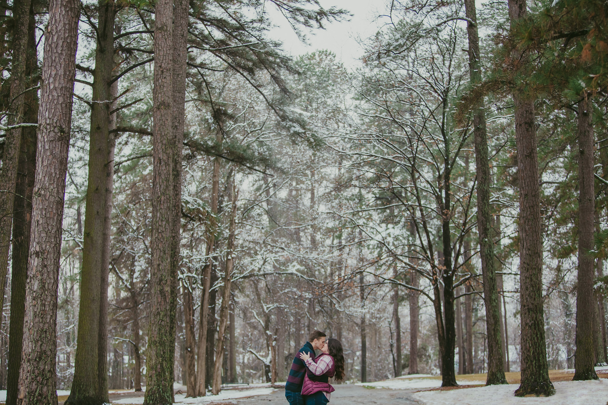 Couple kisses among the snowy pine trees at Mac Anderson Park in Statesville, NC