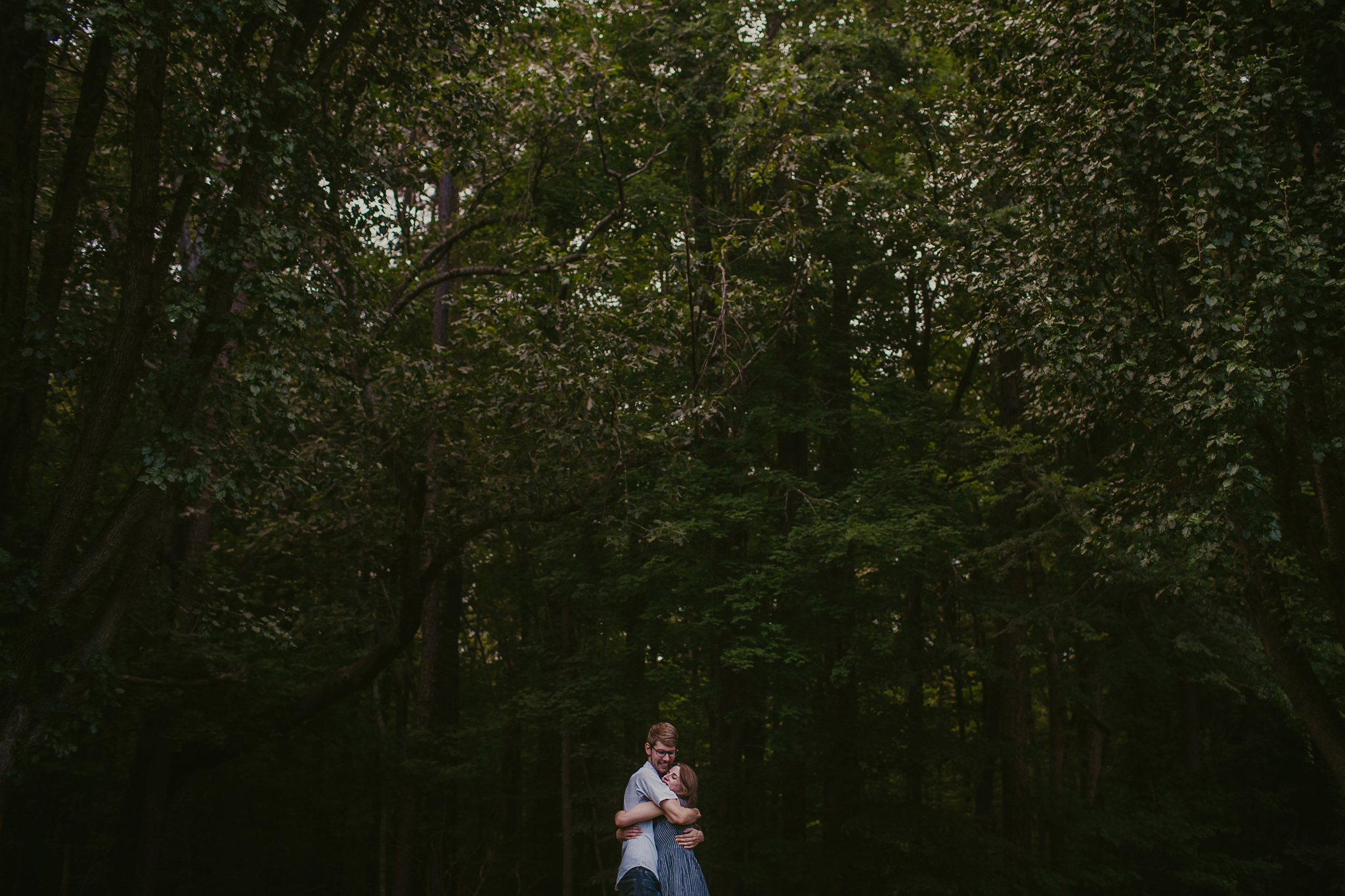 A wide view of a couple hugging at the Timberlake Earth Santuary during their engagement session in Greensboro, NC