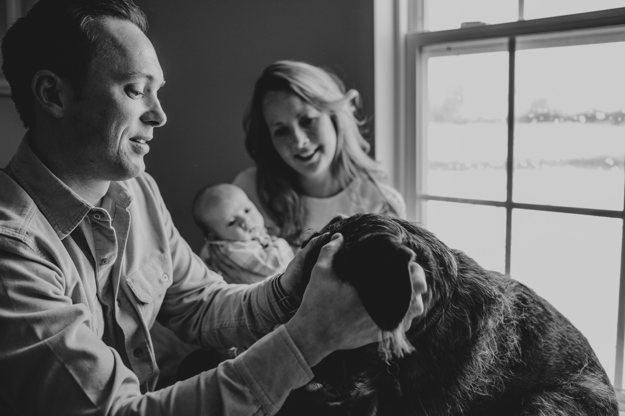 dad pets dog while mom & baby look on
