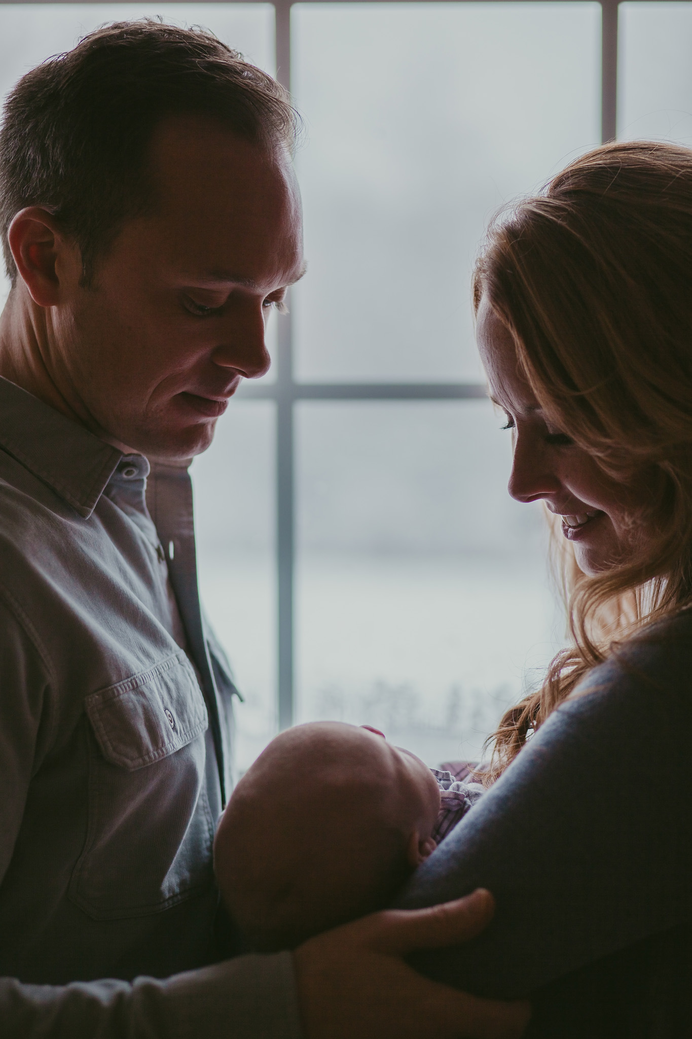 mom and dad hold baby girl in the window light