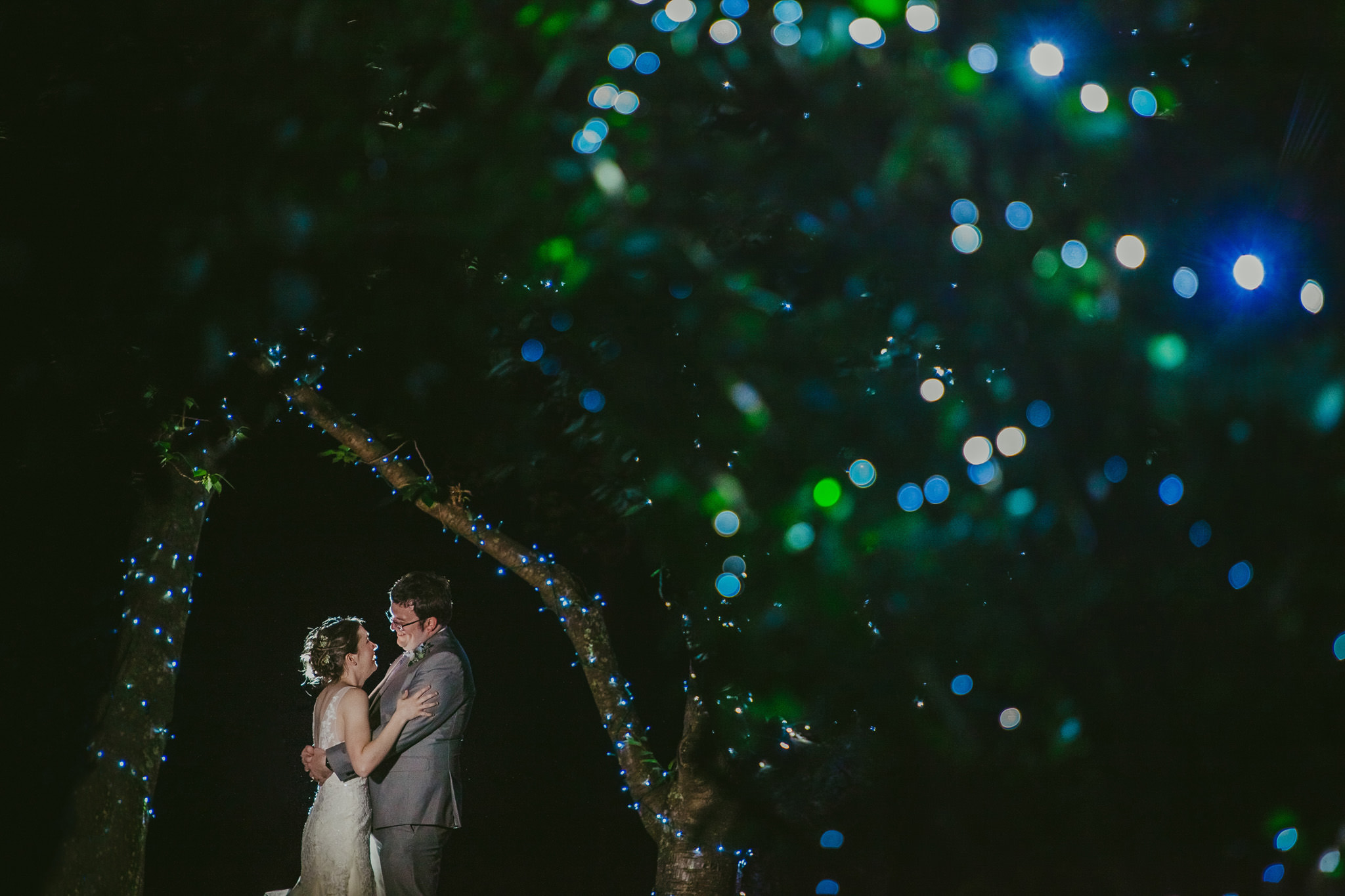 Bride and groom snuggle under the light wrapped trees at the Shuford House in Hickory