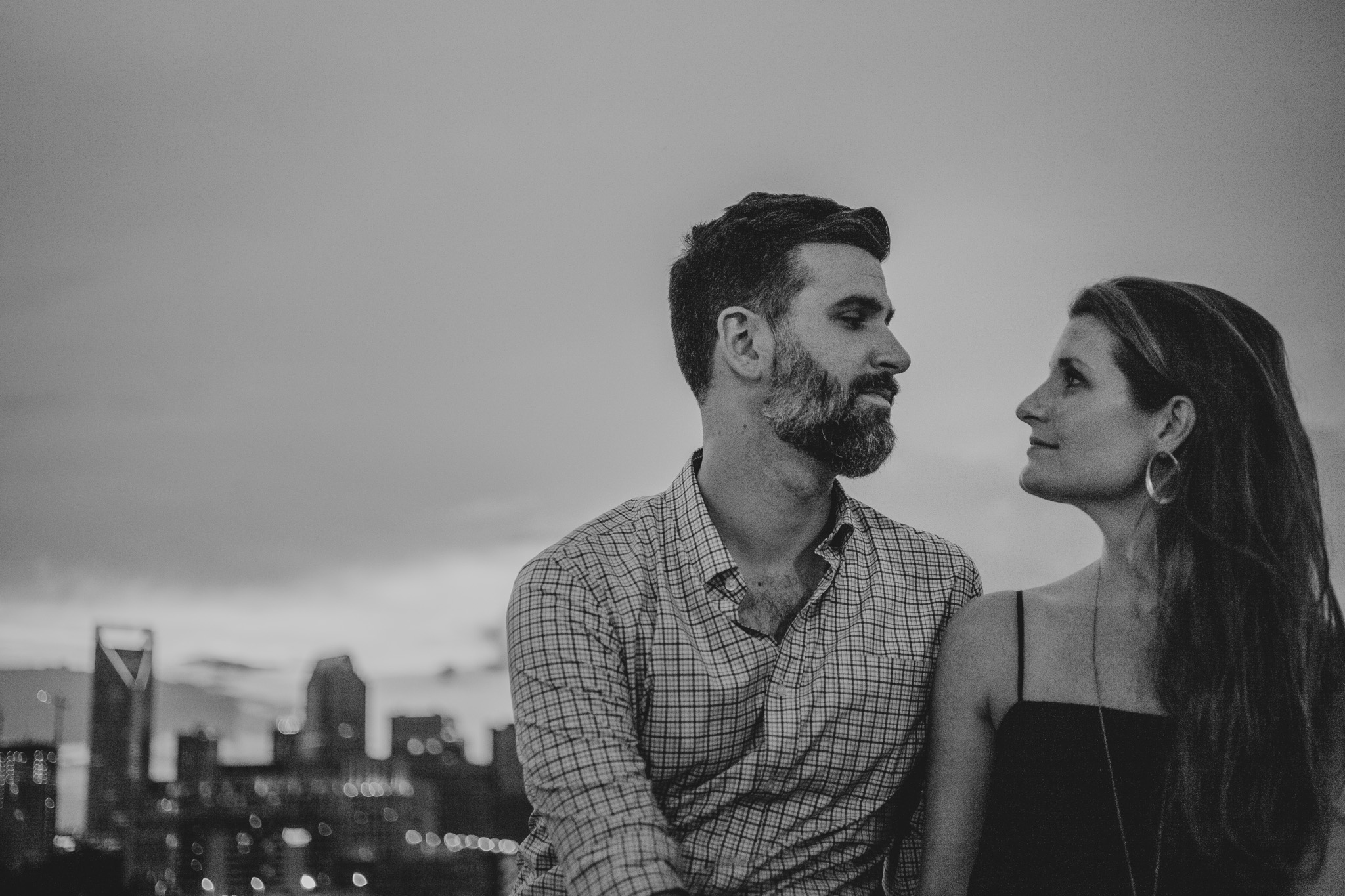 Stephen gazes into Caroline's eyes atop a Charlotte parking deck with the skyline in the background