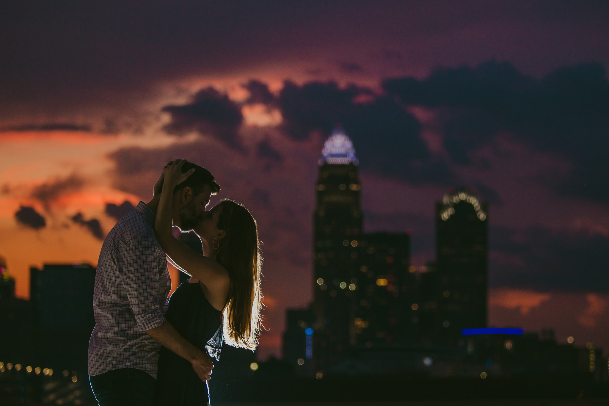 A romantic kiss against a colorful sunset sky in front of the Charlotte Skyline