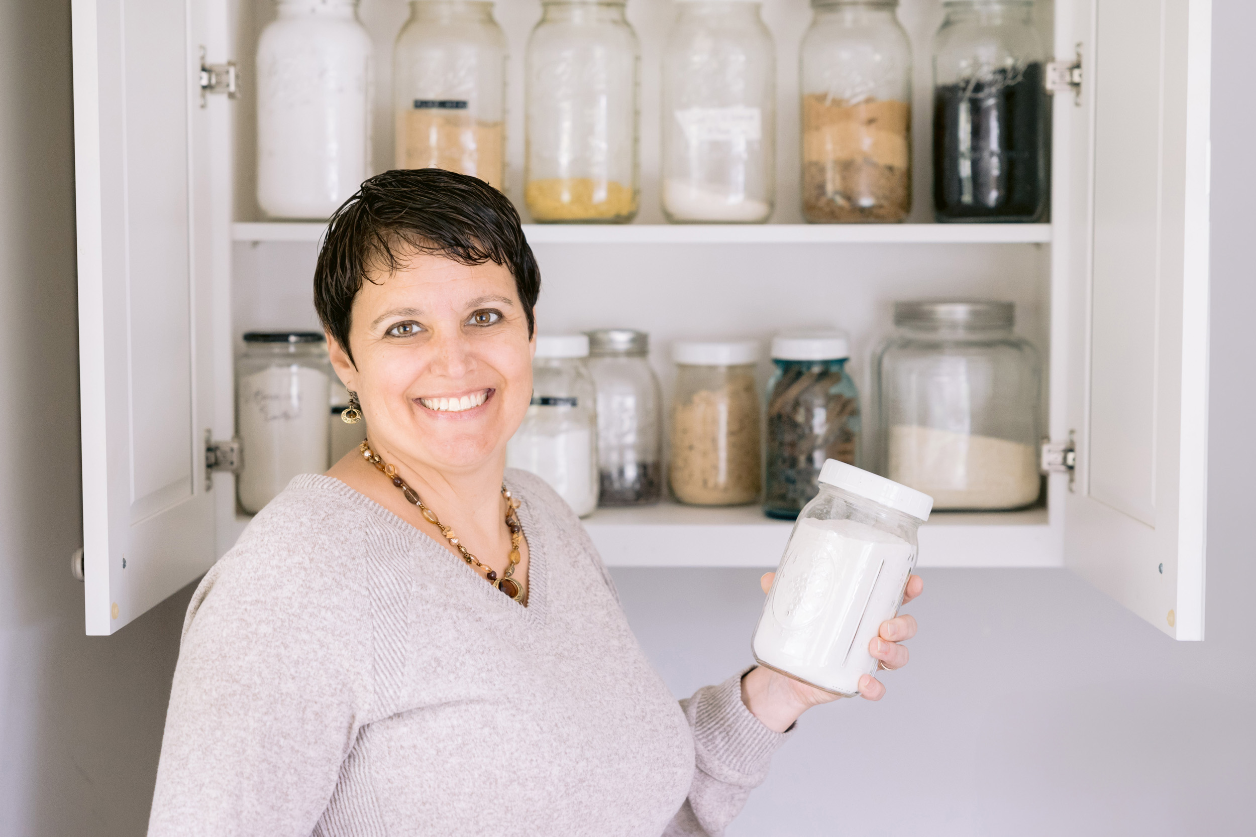 Juliana Kathman, from Organized by Juliana, poses with a jar of flour in hand, surrounded by a shelf of jars. Photo by Mabyn Ludke Photography in Statesville, NC.