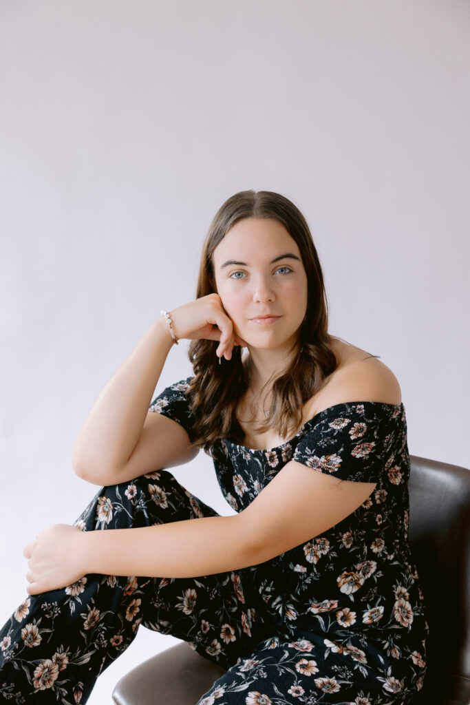 A woman in a floral print jumpsuit sits gracefully on a stool, showcasing a stylish look for professional headshots. What to wear for headshots in Charlotte NC