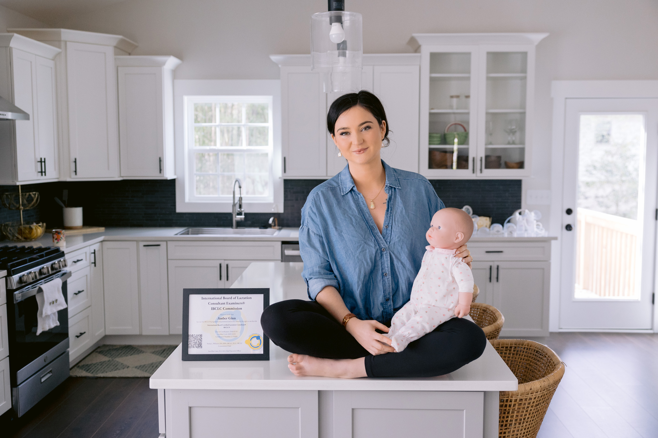 In a warm kitchen, a woman cradles a baby doll, beautifully photographed by Mabyn Ludke for lactation consultant Amber Ginn.