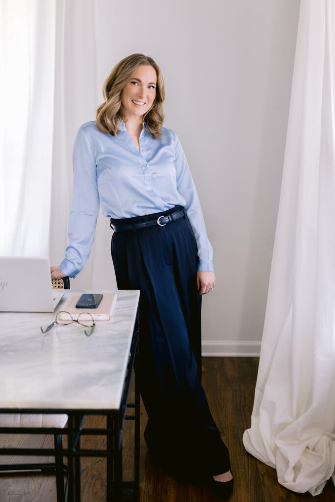 A woman dressed in a blue shirt and pants stands before a desk, exemplifying suitable attire for professional headshots.