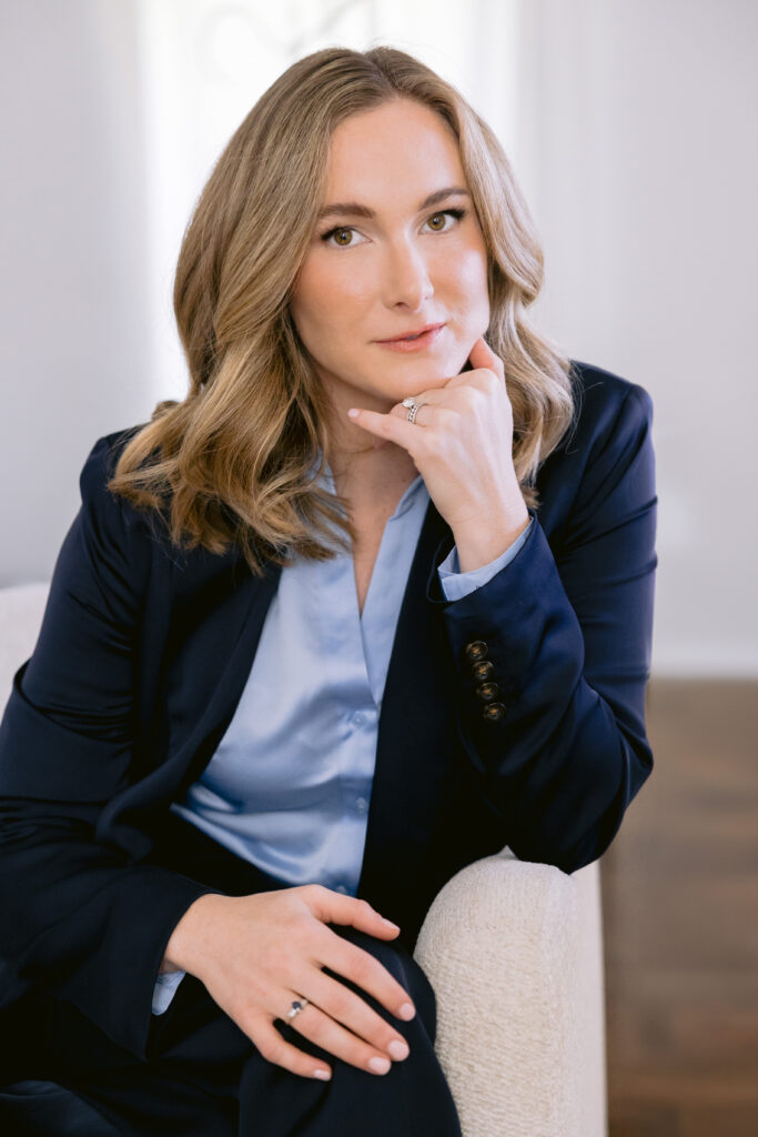 A woman dressed in a blue suit and white shirt sits on a chair, showcasing her personal brand as a financial advisor.