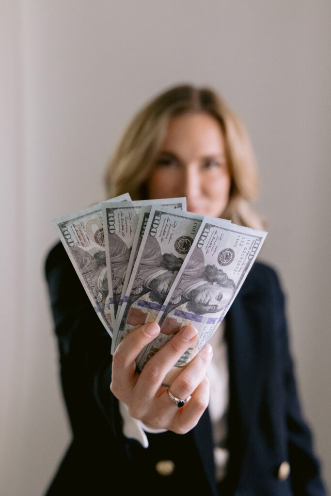 A confident woman in a business suit proudly displays a stack of money during her personal brand photoshoot.