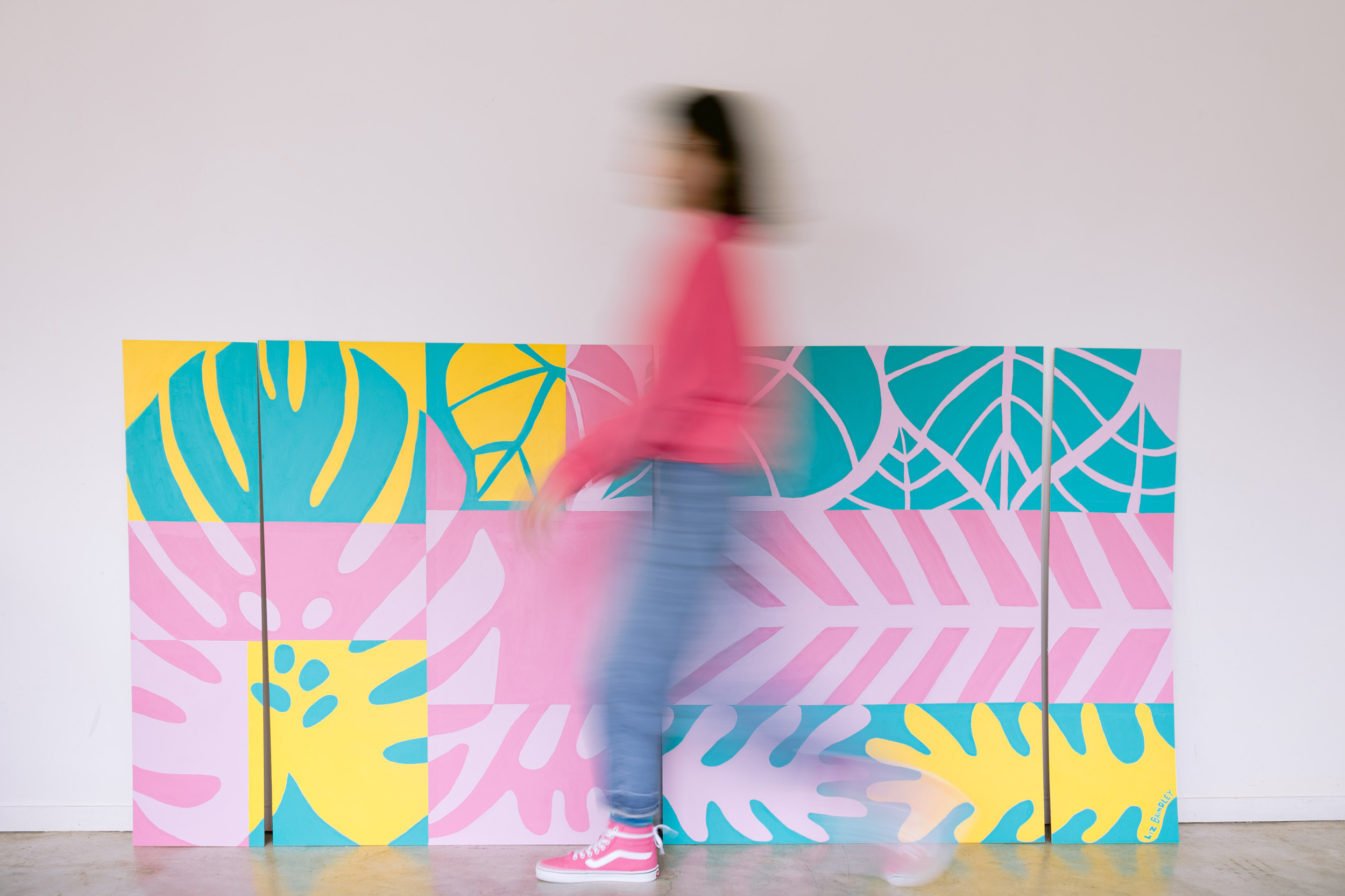 A woman walks in front of a lively, colorful mural, showcasing her style in a personal brand photoshoot by Mabyn Ludke Photography.