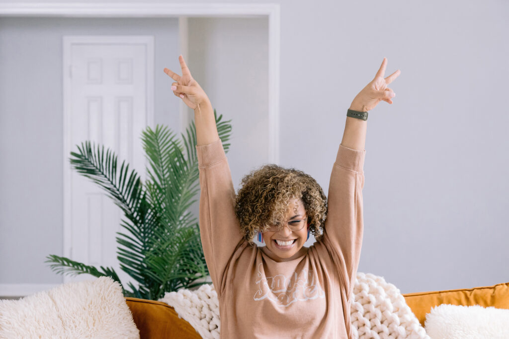 A woman sitting on a couch with arms up, radiating positivity in her personal brand session by Mabyn Ludke Photography.