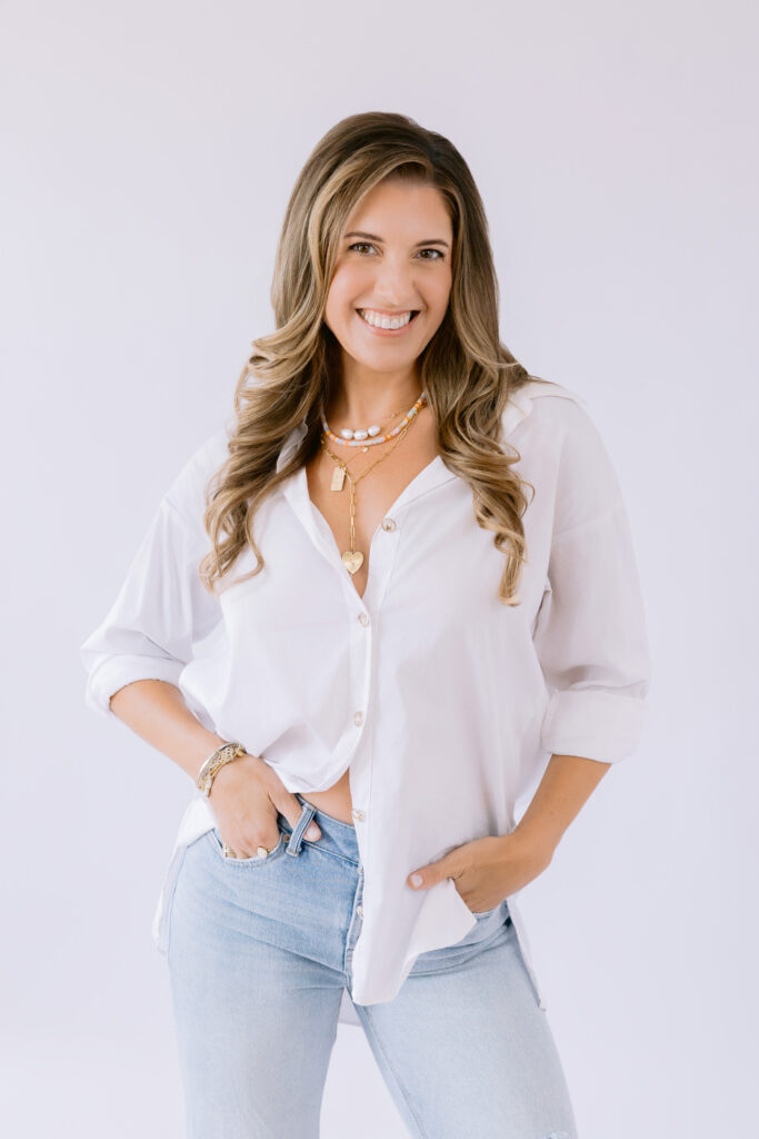 Female creative entrepreneur smiling in a studio setting, wearing a white button-down and jeans during a lifestyle brand photoshoot.