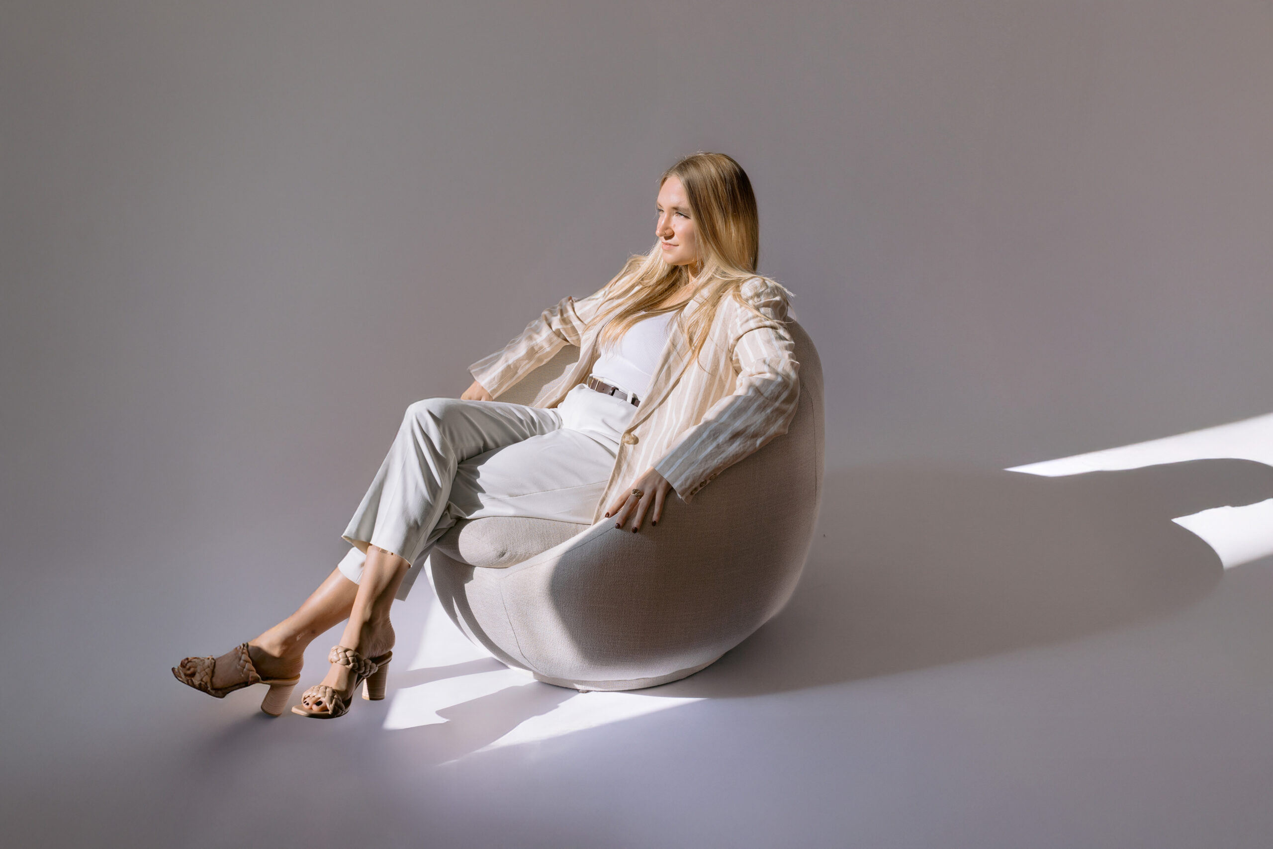 Female entrepreneur sitting in a modern chair with directional studio lighting during a minimalist brand photoshoot.